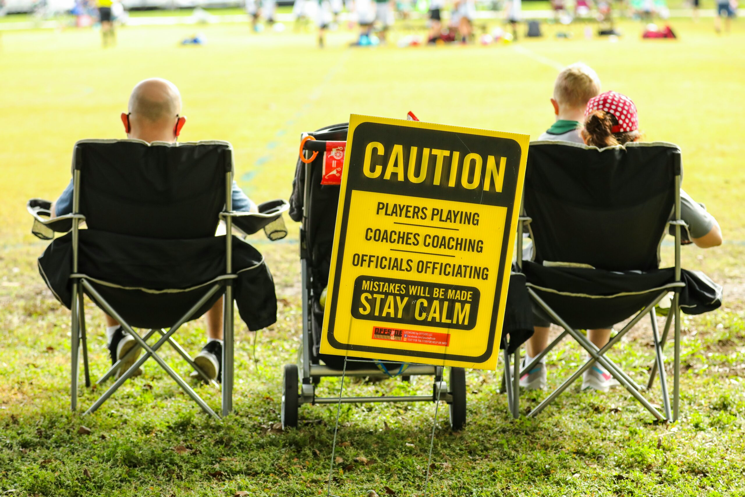 Parents watching a youth match beside a sideline caution sign